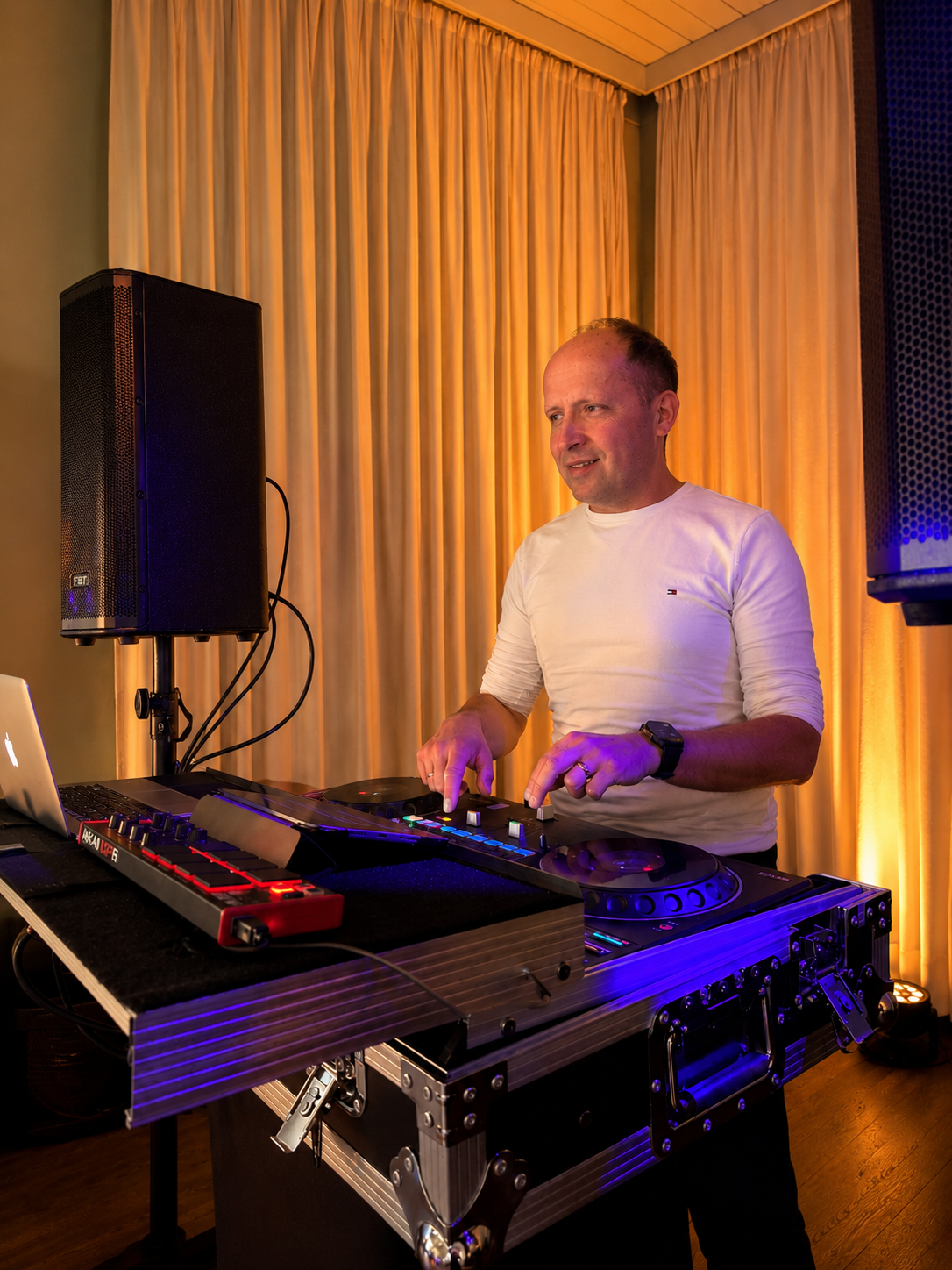 DJ René Marx am Controller mit Lautsprecher und warm beleuchteten Vorhängen